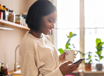 Woman in kitchen looking at phone with big smile on their face